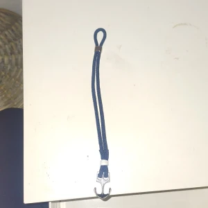 Blått armband med ankardetalj - Snyggt blått armband med en silverfärgad ankardetalj. Armbandet har en enkel design med en ögla för justering. Perfekt för en marin look. De justerbart skriv om du har några frågor eller funderingar 