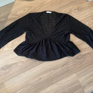 Svart spetsblus från Pigalle M - Svart blus från Pigalle i storlek M med lång ärm och v-ringad front. Blusen har ett snyggt spetsmönster med broderade detaljer och en peplumliknande volang nedtill. Perfekt för dig som gillar en feminin och trendig look.