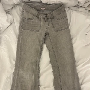 Grå bootcut jeans från Nelly - Snygga grå jeans från Nelly med bootcut passform och hög midja. Jeansen har breda framfickor, dubbla knappar i midjan och coola detaljer på bakfickorna med metallknappar. Perfekt för dig som gillar en avslappnad men trendig stil.