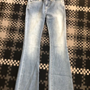 True Religion ljusblå flared jeans - Säljer ett par ljusblå jeans från True Religion med bootcut passform. Jeansen har snygga kontrastsömmar, klassiska fickor med lock och silverfärgade knappar bak. Materialet är jeans och de har en cool faded effekt framtill.