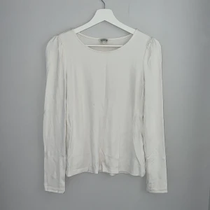 Vit långärmad topp från Indiska - En stilren vit långärmad topp från Indiska i storlek S. Modellen har rund halsringning och lätt puffade axlar som ger en soft touch. Materialet är mjukt och känns skönt mot huden, perfekt för layering eller att bära som den är. Enkel och clean design som funkar till många looks. Liten fläck på framsidan, syns knappt.
