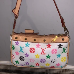Louis Vuitton vit axelväska med färgglatt mönster - Säljer en vit axelväska från Louis Vuitton med färgglatt monogrammönster i rött, rosa, blått, grönt, gult, lila och svart. Väskan har beige detaljer, guldfärgade nitar och dragkedja samt en söt rosett upptill. Perfekt storlek för det viktigaste.
