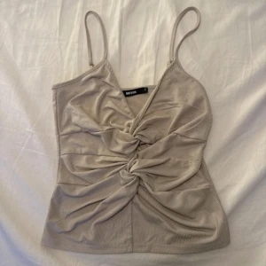 Beige ribbad linnetopp från Bik Bok - Snygg beige linnetopp från Bik Bok med ribbad struktur och twistad detalj framtill. Tunn, mjuk och med smala axelband som ger en fräsch look. Perfekt för dig som gillar stilrena och trendiga toppar med lite extra edge.