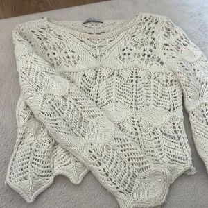 Vit stickad kofta med spetsmönster - Säljer en vit stickad kofta med snyggt spetsmönster och långärmad design. Koftan har en luftig och unik struktur som ger en cool boho-vibe. Perfekt att styla över en topp eller klänning för extra detaljer. Passar dig som gillar stickade plagg med lite edge.