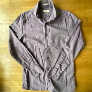 Lila skjorta från The Tailoring Club - Snygg lila skjorta från The Tailoring Club i premium bomull. Klassisk krage, långärmad och med knappar framtill. Skjortan har en stilren look och passar perfekt till dig som gillar en clean och modern stil.