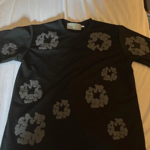 Svart blommig t-shirt från Denim Tears - Svart t-shirt från Denim Tears med coola grå blommönster tryckta över hela plagget. Klassisk rund hals och korta ärmar. Materialet är mjuk bomull. Aldrig använd och är i 10/10 skick 