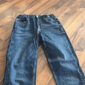 Blå bootcut jeans från Gina Tricot - Snygga blå jeans från Gina Tricot i storlek 164. Modellen har klassisk femficksdesign och bootcut-ben som ger en schysst siluett. Jeansen är tillverkade i jeansmaterial med kontrastsömmar och har en mörk tvätt med lätt slitning. Perfekt för dig som gillar retrovibbar.