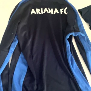Ariana FC långärmad fotbollströja Nike - Snygg långärmad fotbollströja från Ariana FC med Nike-logga och klubbmärke på bröstet. Tröjan är mörkblå med ljusblå paneler längs ärmarna och har tryck med 'stadium' på framsidan. Perfekt för träning eller match!