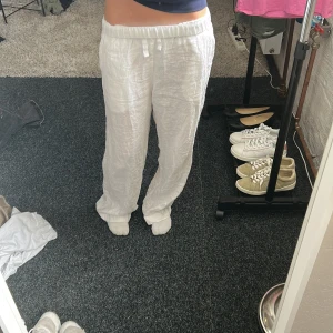 Vita linnebyxor med snörning - Säljer ett par chill vita linnebyxor med elastisk midja och snörning framtill. Byxorna har rak passform och är tillverkade i mjukt linne, perfekta för varma dagar. De har en clean look och passar dig som gillar avslappnad stil. Byxorna ser väldigt stora ut på bilden men passar mig  som oftast bär xs-s. Aldrig använda, nypris 350 men säljer för 100. 