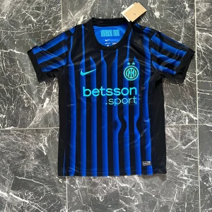 Inter Milan randig fotbollströja Nike S - Snygg Inter Milan fotbollströja från Nike i svart och blått med vertikala ränder. Kortärmad modell med klubbmärke och sponsortryck på bröstet. Tillverkad i lätt och ventilerande polyester, perfekt för match eller träning.