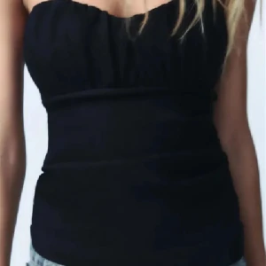 Svart  tubtopp från Zara - Svart bandeau tubtopp från Zara med snygg sweetheart-ringning och lätt rynkade detaljer upptill. Toppen är axelbandslös och har en slim passform som sitter tajt mot kroppen. Perfekt att styla med jeans eller kjol för en cool look.