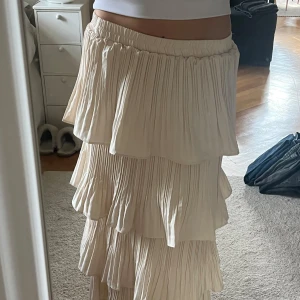 Plisserad långkjol med volanger - Säljer en supersöt plisserad långkjol i ljusbeige med flera lager volanger. Kjolen har resår i midjan och ett flowigt, romantiskt fall. Materialet känns mjukt och lätt 💌💌💌