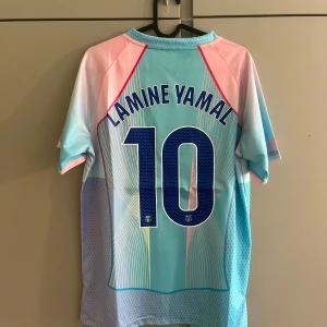 Barça Lamine Yamal #10 Nike fotbollströja - Snygg FC Barcelona fotbollströja med Lamine Yamal och nummer 10 på ryggen. Tröjan har coolt mönster i ljusblått, rosa och vitt, med klubbmärke, Nike-logga och Spotify-sponsor på bröstet. Tillverkad i lätt och ventilerande polyester, perfekt för match eller träning.