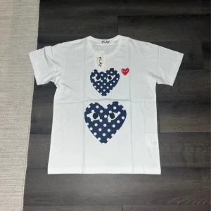 Vit t-shirt Comme des Garçons Play - Snygg vit t-shirt från Comme des Garçons Play med två stora mörkblå hjärtan. Helt oanvänd, med prislappen kvar. | Skick: 10 / 10, helt ny! | Nypris: ~1000 | Vårt pris: 699 | Storlek: M | Tveka inte att höra av er med funderingar eller prisförslag!