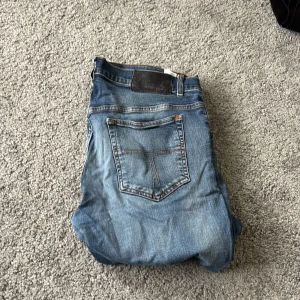 Slim blå jeans i storlek 34/32 - Snygga slim fit jeans i klassisk blå tvätt med slitningar och kontrastsömmar. Modellen har fem fickor och normal midja, passar dig som gillar en smalare siluett. Materialet är jeans med skön stretch för extra komfort. Perfekt för dig som vill ha en modern look.