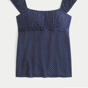 Mörkblå prickig blus från Hollister - Supersöt mörkblå blus från Hollister som jag köpte i USA  med vita prickar och korta ärmar. Toppen har en smockad överdel, markerad midja med ett satinband som knyts i ryggen och en fyrkantig ringning. Perfekt till jeans för en chill och trendig look. Säljer den då den inte har kommit till användning.