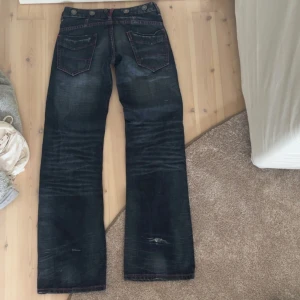 bootcut jeans med rosa sömmar - Säljer ett par mörkblå jeans med bootcut passform och coola rosa kontrastsömmar. Jeansen har stora bakfickor med snygga detaljer och slitningar för en edgy vibe. Klassisk knappstängning och dragkedja framtill. Perfekta för dig som gillar streetstyle.
