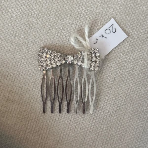 Glittrig hårkam med stenar - Superfin hårkam i silverfärg med en glittrig rosett täckt av stenar. Perfekt accessoar för att ge frisyren extra bling. Rosetten är täckt av små gnistrande stenar och kammen har en elegant form.