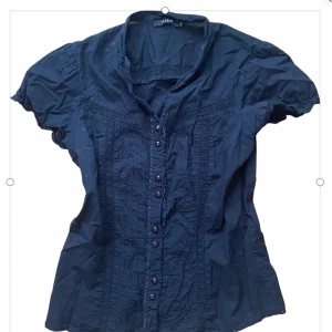 Svart kortärmad skjorta från Vila! - Supersöt svart blus/skjorta från Vila med korta ärmar och snygga knappar framtill 💗 Skjortan har dekorativa sömmar och spetsdetaljer längs bröstet och ryggen. I strl S