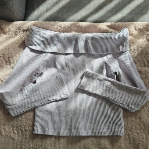 Ljusgrå ribbad offshoulder topp - Superfin ljusgrå ribbad topp med offshoulder och långa ärmar. Materialet är mjukt och stretchigt.
