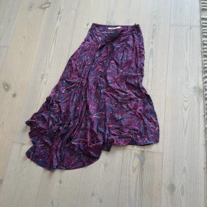 Paisleymönstrad långkjol Rue de Femme - Långkjol från Rue de Femme med paisleymönster i lila, rosa och blå toner. Kjolen har en flowy och asymmetrisk form som ger en cool och avslappnad vibe. Perfekt för dig som gillar färg och mönster. Materialet känns lätt och mjukt mot huden.