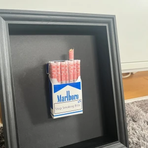 Stop Smoking Bills - En unik konstbok med ett kreativt och tankeväckande motiv: en cigarettask fylld med rullade 500-kronorssedlar. Perfekt för dig som gillar modern konst med humor och samhällskritik. Passar som cool inredningsdetalj eller present till någon som vill sticka ut.