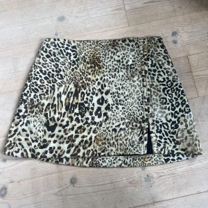 Leopardmönstrad kortkjol med slits - Snygg kortkjol med leopardmönster i beige, brunt och svart. Kjolen har en liten slits framtill som ger en extra edge. Perfekt för dig som vill sticka ut och gillar djurmönster. Materialet känns lätt och smidigt, passar till många olika stilar. Se bilder där det finns lite trådar 