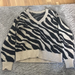 Zebramönstrad stickad tröja med v-ringning - Snygg stickad tröja med zebramönster i svart och beige. Tröjan har v-ringad hals och ribbade muddar vid ärmslut och nederkant. Perfekt för dig som vill sticka ut med ett djurinspirerat mönster och samtidigt hålla dig varm. Vet ej storlek men passar mig som är XS/S💕💕