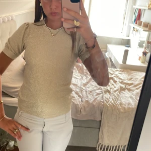 Glittrig beige topp med puffärm - Säljer en beige glittrig topp med korta puffärmar och rund hals. Toppen har en slim passform. Perfekt att styla med smycken. Materialet känns mjukt och stretchigt.