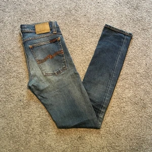 Nudie Jeans Blå W25 L32 - Säljer ett par klassiska blå slim jeans från Nudie Jeans med snygga slitningar och sömmar. Perfekta för dig som gillar en smal passform och stilren look | Storlek: W25 L32📏| Nypris: ca 1100 | Perfekta nu till sommaren samt skolstarten! Hör gärna av er om ni har några frågor eller prisförslag!💬☺️