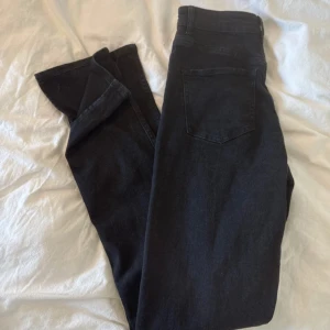 Svarta bootcut jeans med hög midja - Snygga svarta jeans med bootcut och hög midja. Jeansen har klassisk femficksdesign, bälteshällor och dragkedja med knapp framtill. Materialet är jeans och passformen är normal med lite utsvängda ben. Perfekta för dig som gillar en stilren look med lite edge.