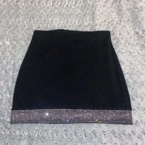 Svart kortkjol med glittrig kant - Supersnygg svart kortkjol med en glittrig kant av silvriga paljetter längst ner. Kjolen har en slim passform och dragkedja bak för enkel på- och avtagning. Perfekt för dig som vill sticka ut med lite extra bling i outfiten. / aldrig använd för den sticker ut lite från min stil🤗