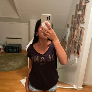 Svart t-shirt BLANC Paris v-ringad - Svart t-shirt från BLANC Paris med v-ringning och tryck framtill. Modellen är kortärmad och har en loose passform som sitter skönt. Materialet är mjuk bomull och t-shirten är enkel att matcha med jeans eller shorts.