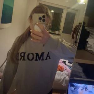 Grå sweatshirt med svart text - Säljer en chill grå sweatshirt med svart texten 'AMORE' över bröstet. Tröjan har en loose passform och långa ärmar, perfekt för att mysa i eller styla med jeans. Materialet känns mjukt och skönt mot huden. passar mig med xs🩷