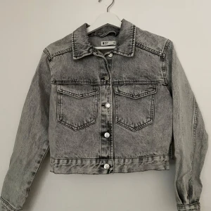 Grå jeansjacka från Gina Tricot XS - Snygg grå jeansjacka från Gina Tricot i modellen 'Trucker denim jacket'. Jackan har klassisk krage, två bröstfickor med lock och knappar framtill. Materialet är slitstarkt denim och färgen är en tvättad gråton. Nypris 399kr