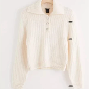 Vit ribbad stickad polotröja från Linox - Vit stickad polotröja från Linox med ribbad struktur och tre snygga knappar framtill. Tröjan har en bred krage och långa ärmar, perfekt för att hålla dig varm och stilren under kyliga dagar. Enkel att matcha med jeans eller kjol för en clean look.