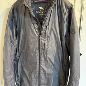 Grå dunjacka från Snoot Stockholm - Snygg grå dunjacka från Snoot Stockholm i storlek M. Jackan har en stilren design med dragkedja framtill, ståkrage och en diskret bröstficka med zip. Materialet är lätt och passar perfekt till vår/höst.