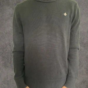 Svart stickad tröja Morris S - Svart stickad tröja från Morris i storlek S. Tröjan har rund hals, ribbade muddar och ett litet broderat emblem på bröstet. Klassisk och enkel design som funkar till många olika stilar. Materialet är mjukt och skönt stickat.