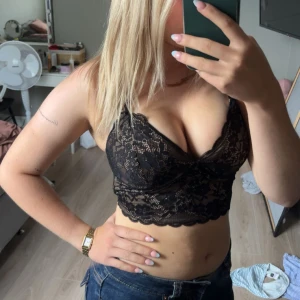 Svart spetsig topp - Säljer en svart -topp med blommig spets och croppad passform. Toppen har tunna axelband! Perfekt för dig som vill ha en snygg och feminin look med lite edge. Spetsen är genomskinlig💞