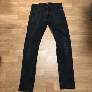Replay jeans  - Snygga svarta Replay Anbass jeans med klassisk femficksdesign och raka ben. Jeansen har en diskret logga på bakfickan och är tillverkade i mjukt jeansmaterial med stretch för extra komfort. Passformen är slim och midjan är normal. Perfekta för dig som gillar stilrena och moderna jeans. Lite skavanker i skrevet och på ett av benen ingeting man ser vid användning 