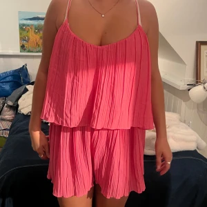 Plisserad rosa byxdress med tunna axelband - Säljer en superfin plisserad byxdress i stark rosa färg med tunna axelband. 