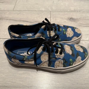 Blommiga Vans sneakers med blå bas - 🌸 Säljer ett par Vans sneakers med blå tygbas och stora vita blommor. Skorna har svart snörning och klassisk Vans-logga baktill. Ytterst lite använda och i väldigt bra skick 🌸