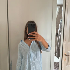 Ljusblå blus med prickigt mönster - Säljer en ljusblå blus med små prickar över hela. Blusen har v-ringning, knappar framtill och trekvartsärmar.