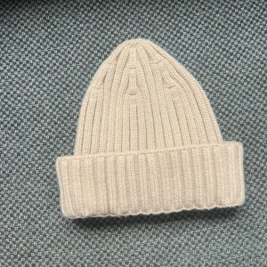 Två ribbstickade mössor i rosa och beige - Säljer två ribbstickade mössor med bred uppvikt kant. En i ljusrosa och en i beige, båda i mjukt stickat material. Perfekta för kalla dagar och ger en chill vibe till din outfit.