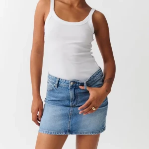 Blå jeanskjol från Gina Tricot - Snygg blå jeanskjol från Gina Tricot med klassisk femficksdesign, knapp och dragkedja framtill samt coola bakfickor med lock. Perfekt för dig som gillar en enkel men trendig look. Liten sliten detalj längst ner för extra edge. Köpte förra året men har aldrig använts. 
