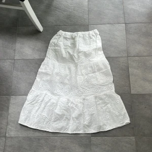 Vit broderad långkjol Made in Italy - Superfin vit långkjol med broderade blommor och elastisk midja. Kjolen har ett romantiskt hålmönster och är sydd i flera volanger för extra flow. Perfekt för varma dagar och ger en riktigt fräsch sommarkänsla.