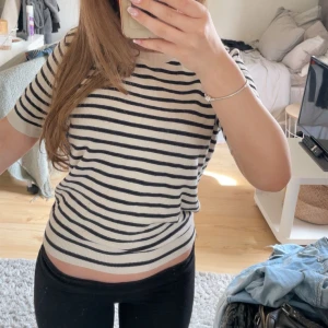 Randig kortärmad tröja från H&M - Säljer en beige och svart randig tröja från H&M. Tröjan har korta ärmar, rund halsringning och är i mjukt stickat material. Perfekt för en avslappnad och stilren look.