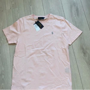 Ljusrosa t-shirt från Polo Ralph Lauren - Säljer en ljusrosa t-shirt från Polo Ralph Lauren med klassisk passform och liten broderad logga på bröstet. T-shirten har rund halsringning och korta ärmar. Perfekt basic-plagg till garderoben.