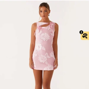 Rosa blommig kortklänning med rosett - Superfin rosa kortklänning med vita blommiga broderier och rosett-detaljer på axeln. Klänningen har en tight passform och är ärmlös, perfekt för sommarens alla tillfällen. Söt och trendig design som verkligen sticker ut. Endast testad. Prislappen är kvar. 💓💕🌸