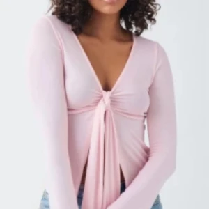 Ljusrosa omlottopp med knyt - Supersöt ljusrosa omlottopp med lång ärm och djup v-ringning. Toppen har en snygg knytning framtill som ger en trendig look. Perfekt att styla med jeans eller kjol för en cool vibe.